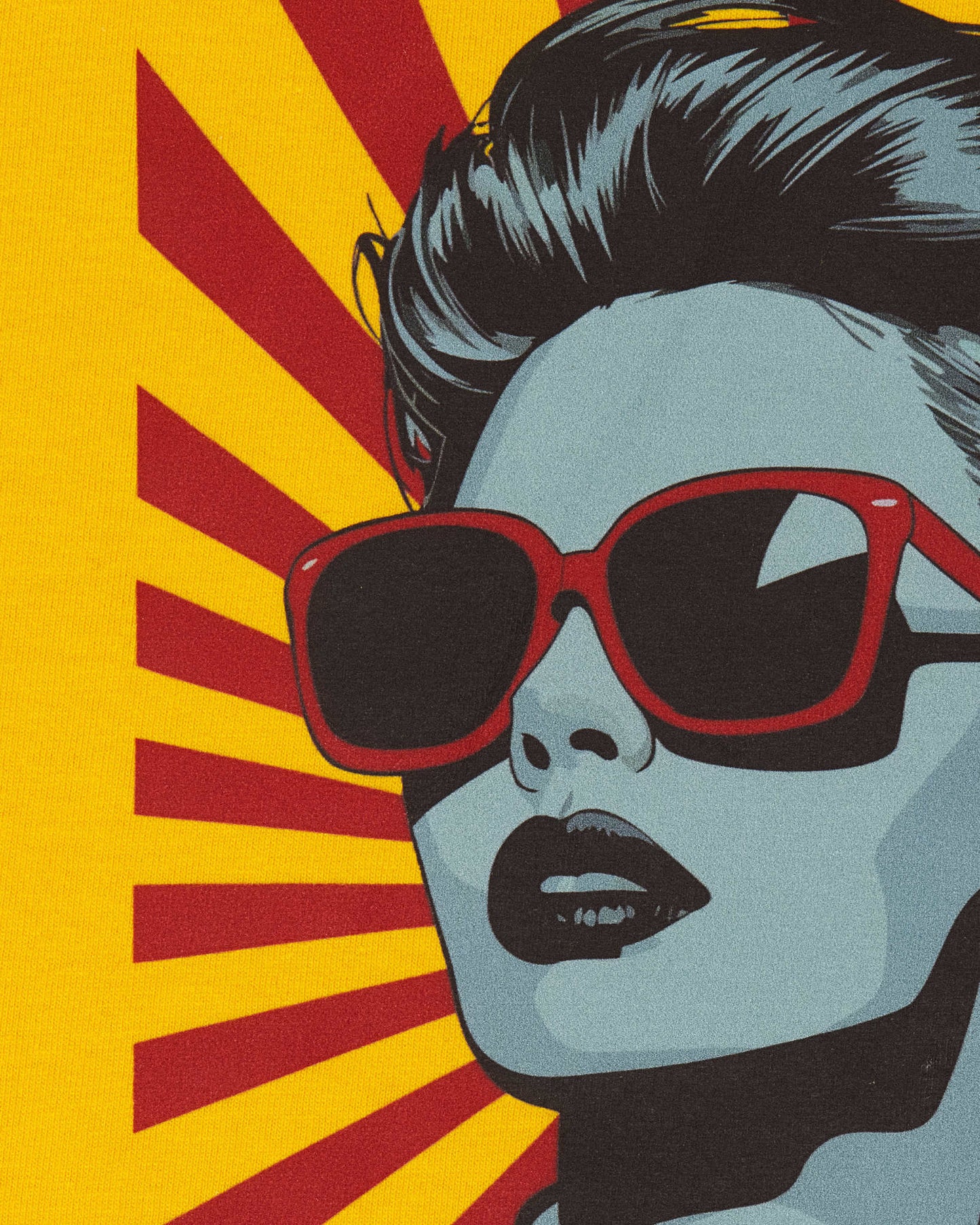 An extreme close-up of the graphic print on a yellow t-shirt, showing the fabric texture and fine details of the retro pop-art illustration, focusing on the woman's face, bold red sunglasses, and dark lips.